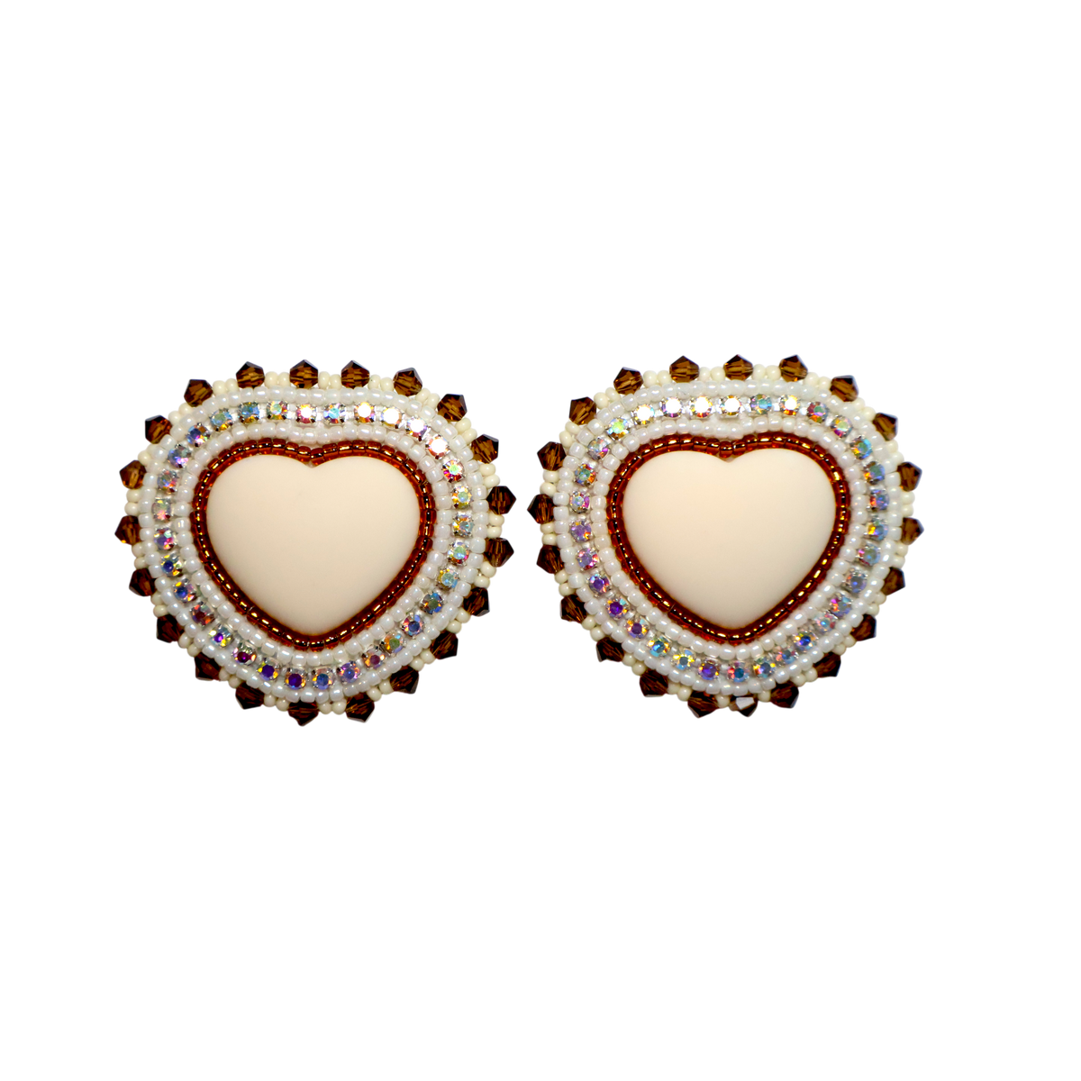A pair of heart-shaped stud earrings featuring a cream-colored center heart surrounded by a red beaded border and a halo of iridescent rhinestones, set against a plain white background.