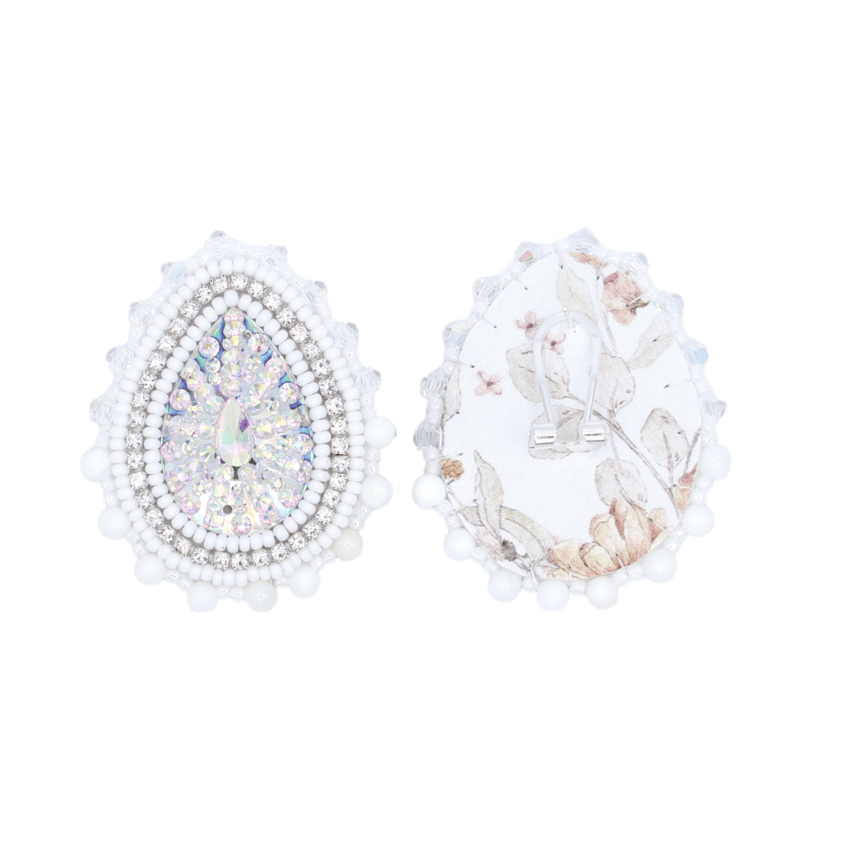 A pair of teardrop-shaped silver earrings with white pearl borders, one decorated with iridescent rhinestones and the other with a white floral print, shown on a plain white background.